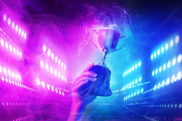 Photo of Trophy with smoke effect holding on hand and background blue and violet light for e-sport winner event.