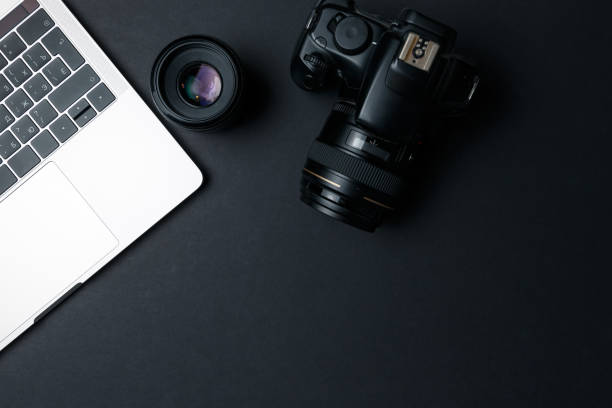 Photographer's workplace on a dark background. Modern laptop, digital camera, lens, battery, smartphone. Minimalism. Top view. Copy space. Equipment for the photographer. The concept of freelancing