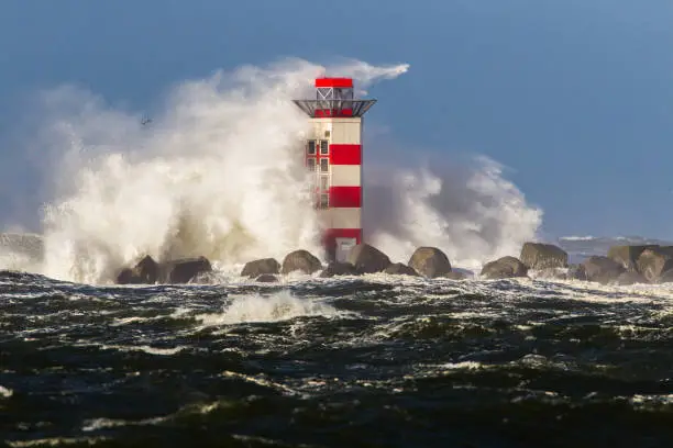 Big waves crashing against the lighthouse at the tip of the pier of Ijmuiden, Netherlands, during severe storm over the North Sea.