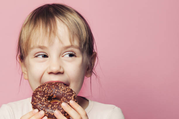 istock Child girl biting donut and looking aside on pink background 1208154817