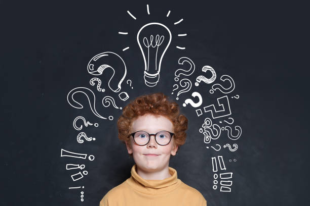 istock Redhead kid with lightbulb and question marks on blackboard background. Brainstorming and idea concept 1208154949