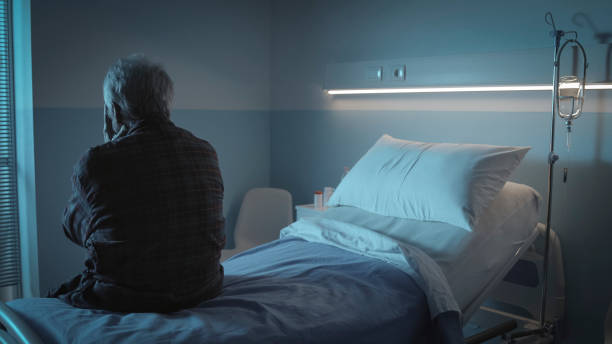 Sad lonely senior sitting in a hospital bed Sad lonely senior sitting in a hospital bed back view, senior care and hospitalization concept night hospital bed stock pictures, royalty-free photos & images