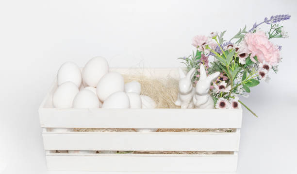 istock White porcelain Easter bunny with white eggs and flowers in wooden white box on white background 1208157775