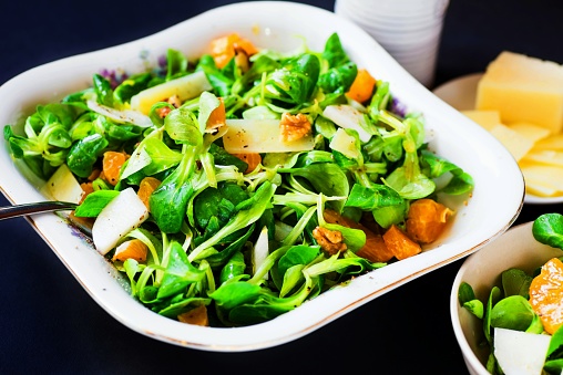 Salad bowl with green leaf, walnuts and tangerine, small bowl with salad, butter and crucibles on table, close-up.