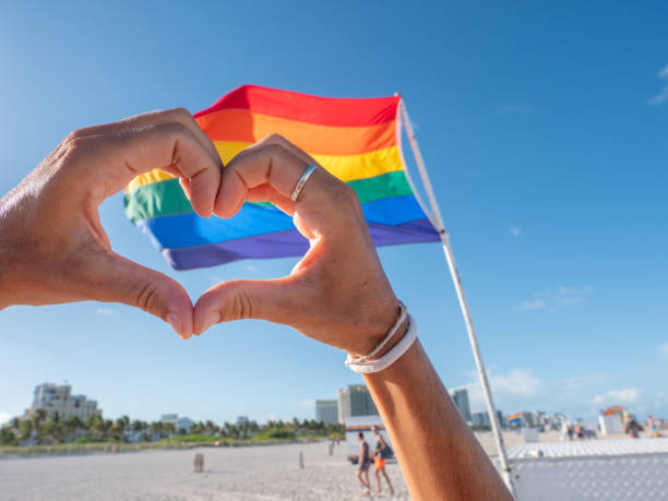 Cute girl on beach making heart shape with hands near rainbow gay flag on beach in Miami