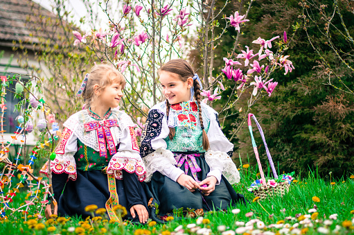 girls in embroided colorful traditional slovakian costume during Easter holiday with basket full of eggs in beautiful spring nature