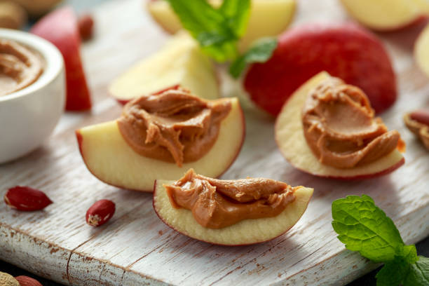 erdnussbutter und apfel zum snack. auf weißem holzbrett - peanut food snack healthy eating stock-fotos und bilder