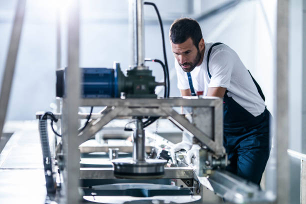 mittlere erwachsene arbeiter arbeiten an einer produktionslinie in einer fabrik. - industriearbeiter stock-fotos und bilder