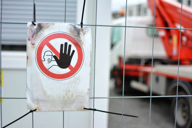 'Keep out' warning sign with person holding up hand in red circle at fence protecting construction site with blurry background