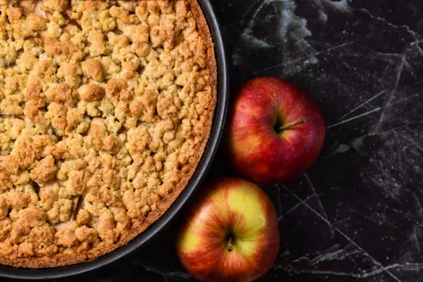 Photo of European apple pie with topping crumbles in springform pan on right side and blank copy space on black marbel background to left side