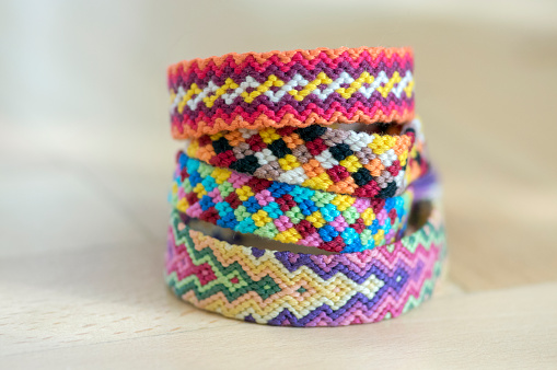 Group of simple handmade homemade natural woven bracelets of friendship on wooden background, rainbow colors, checkered pattern, one by one