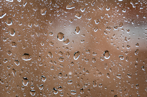 Raindrops on a glass window with house windows blurred
