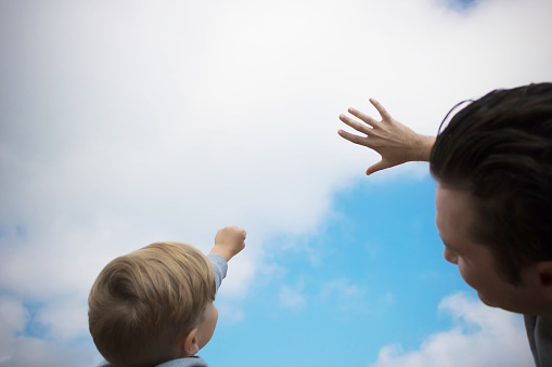 Low angle view of father and son reaching out for the sky. Copy space.