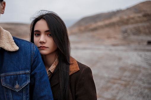 Dramatic portrait of a young brunette girl in cloudy weather standing behind a guy on the background of mountains. selective focus, small focus area