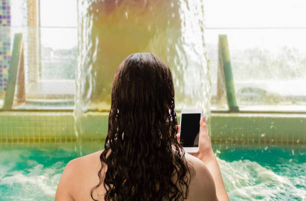 woman relaxing and looking at a phone in the pool in a spa center - water human hand stream clean imagens e fotografias de stock