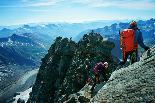 guided group of tourists with safety gear climbing Grossglockner mountain Grossglockner, Austria - August 10, 2019: Group of climbing people with mountain equipment and safety gear in front of a stunning alpine mountain landscape on top of the Grossglockner mountain. The highest mountain of Austria is one of the most famous spots in the Alps. Almost every day groups of people starting early in the morning with one or two guides to climb up the rocky and sometimes frozen trail crossing a glacier. Hoping to get a clear view at a tremendous natural scene. Guided tourists close to the top of the mountain. XXXL (Sony Alpha 7R) grossglockner stock pictures, royalty-free photos & images