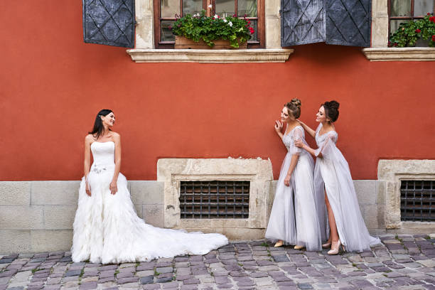 belle mariée et demoiselles d’honneur dans les robes élégantes élégantes élégantes de longueur de plancher argenté gris clair dans la vieille belle ville européenne ayant l’amusement un jour de mariage. - wedding suit photos et images de collection