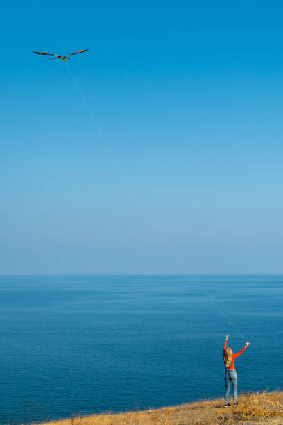 Girl on a mountainside by the sea launches a kite on a sunny day