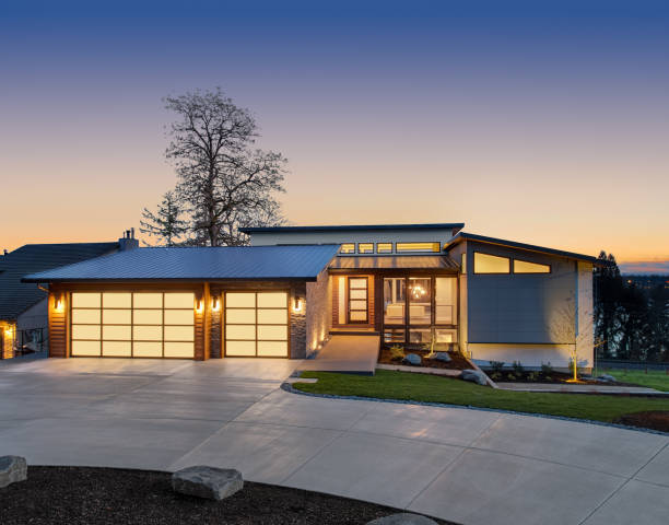 Beautiful modern luxury home exterior at sunset. Features contemporary design and three car garage facade of home with manicured lawn, and backdrop of trees and dark blue sky mansion photos stock pictures, royalty-free photos & images