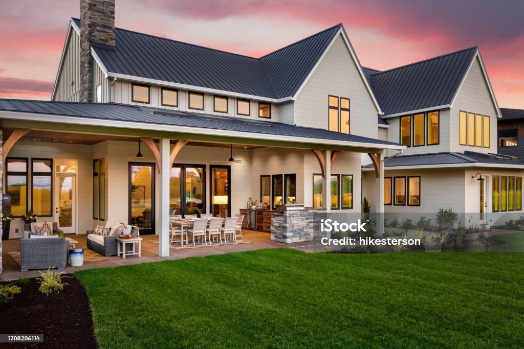 Beautiful luxury home exterior at sunset, featuring large covered patio with outdoor kitchen and barbecue facade of home with manicured lawn and large covered patio Residential Building Stock Photo