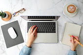 Flat lay workspace. Woman hand with coffee cup, smartphone, computer, notebook, planner and stationary with copy space on marble table background. Top view. modern style.