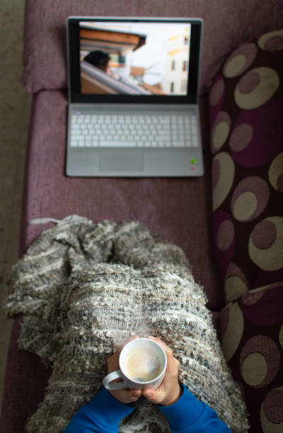 istock Woman sitting on a sofa with a coffee cup and covered with a blanket watching a serie or video on a laptop. 1208221207