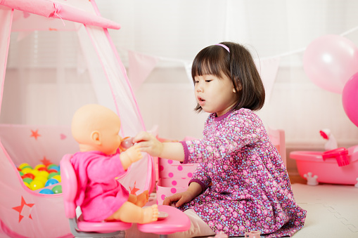 toddler girl pretend play baby care at home against white background