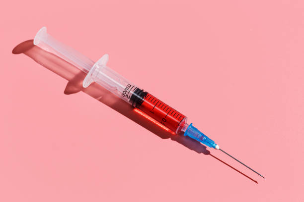 istock Syringe with red vaccine on pink background. Closeup flat lay 1208227525