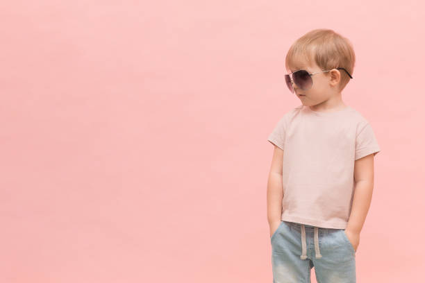blond europejski chłopiec dziecko stoi w okularach przeciwsłonecznych i wygląda na lewo na różowym tle. - fashion male beauty confidence elegance zdjęcia i obrazy z banku zdjęć