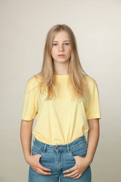 Studio portrait of a teenager girl on a beige background Studio portrait of a blonde teenager girl with long hair in a yellow T-shirt and blue jeans on a beige background 15 year old blonde girl stock pictures, royalty-free photos & images