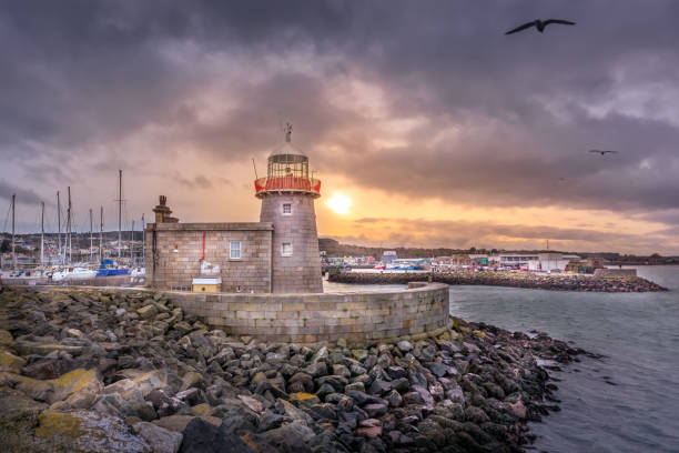 Howth Lighthouse with flying seagulls at beautiful sunset. Yachts and sailboats in harbour, Dublin, Ireland