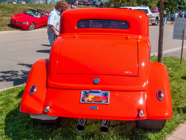 1934 Ford "3 window coupe" hot rod Moncton, New Brunswick, Canada - July 11, 2009 : 1934 Ford "3 window coupe" hot rod at  Atlantic Nationals Automotive  Extravaganza Centennial Park. A man stands near the engine bay giving it a look over. 1934 stock pictures, royalty-free photos & images