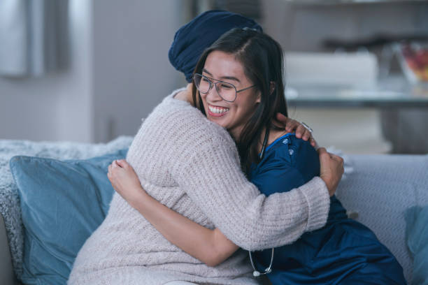 Nurse embracing patient A home health nurse is making a house call. The young medical professional is of Asian descent. She is visiting a patient who has cancer. The two women are sitting on a couch and are embracing. The nurse is smiling. filipino ethnicity photos stock pictures, royalty-free photos & images