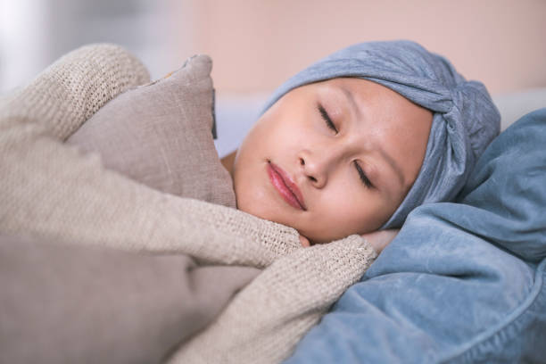 Close up shot of a young Filipino woman fighting cancer. She is wearing a headscarf to hide hair loss from chemotherapy treatment. The woman is relaxing at home. She is taking a nap on a couch and is embracing a pillow.