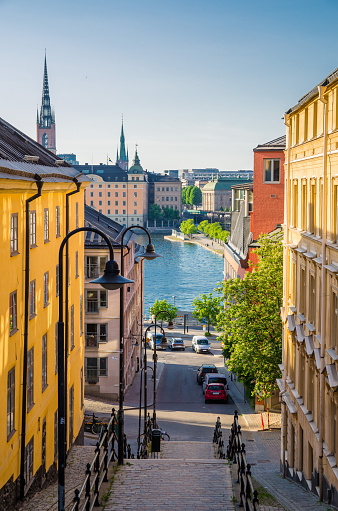 Narrow Street staircase down to Lake Malaren water in Sodermalm island disrict with traditional typical buildings and view of Gamla Stan and Riddarholm Church spire, Stockholm, Sweden