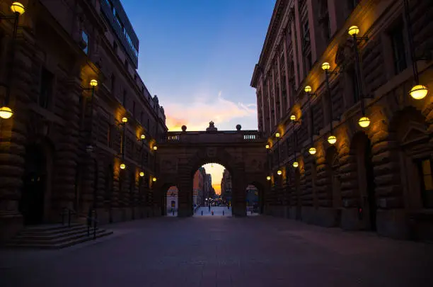 Courtyard between arches of Parliament House Riksdag (Riksdagshuset) with street lights lamps on buildings at sunset, dusk, twilight, evening, Stockholm, Sweden
