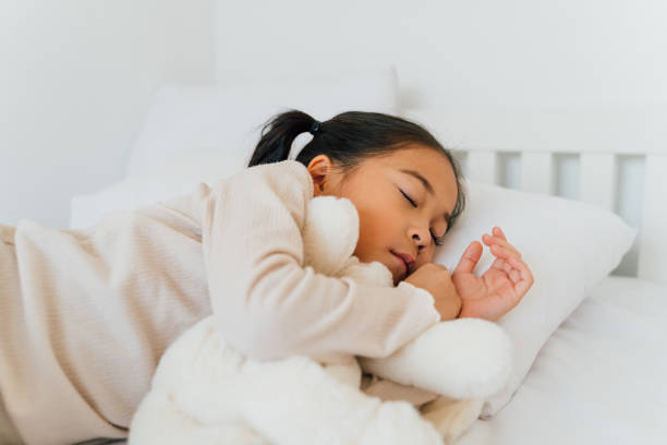 Asian preschooler sleeping on bed at home Charming Asian girl in casual wear with closed eyes hugging stuffed toy lying on bed sleeping in bedroom at home japan small apartment stock pictures, royalty-free photos & images