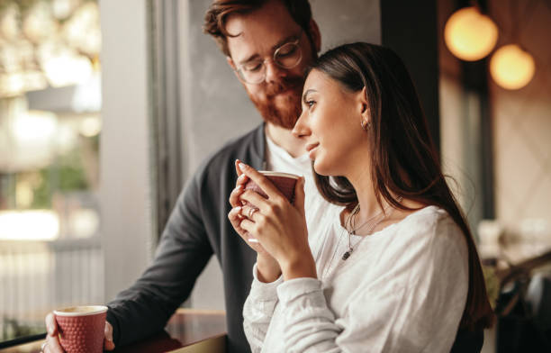 istock Thoughtful woman with disposable cup standing near window with amorous man 1208245528