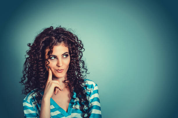 daydreaming, thinking. young beautiful playful curly woman with cunning tricky glance smiling looking up to right side over blue background. - stripped shirt imagens e fotografias de stock