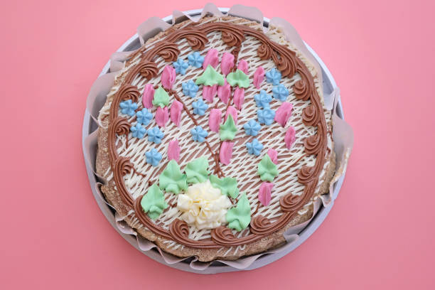 Cake decorated with butter cream top view. Round cake with nuts with roses and cream flowers. Tasty Kiev cake on a pink background.