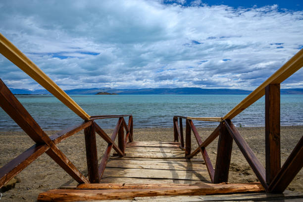 Calm scene with wood pier and stairs heading towards tourquise lake over natural sand and mountains in the background