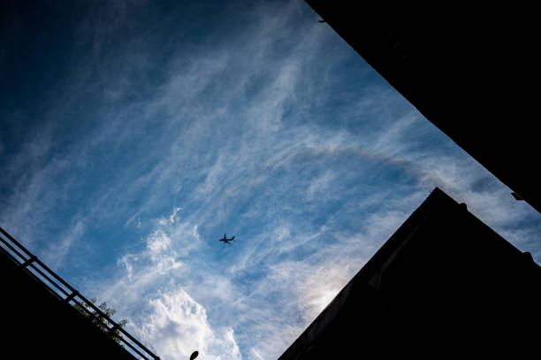 Buildings silhouette looking above to blue skies with light clouds and sun light with an airplane silhouette flying by