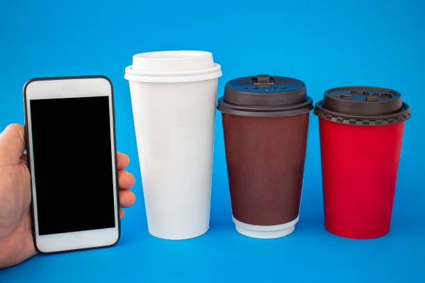 istock A person holding a smart phone with Single Use Coffee Cup next to it on a blue background. 1208269960