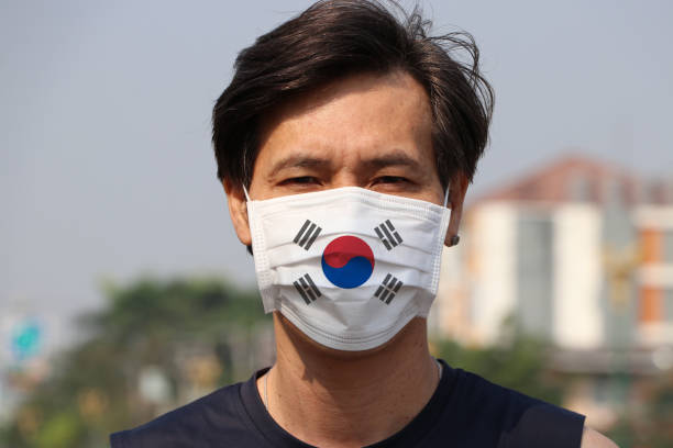 South Korea flag on hygienic mask. Masked Asian man prevent germs. concept of Tiny Particle protection. stock photo