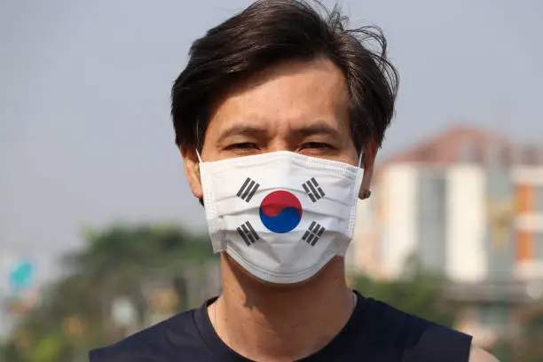 Photo of South Korea flag on hygienic mask. Masked Asian man prevent germs. concept of Tiny Particle protection.