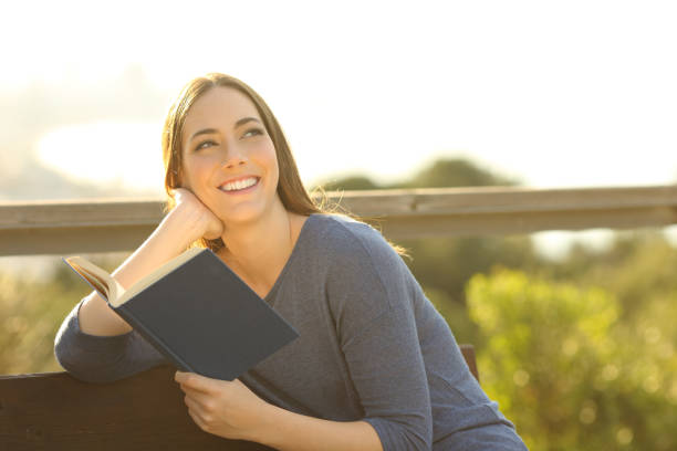istock Happy woman holding a book thinking looking at side at sunset 1208292886