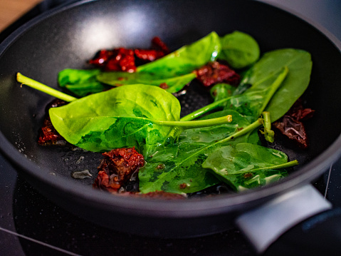 Sun dried tomatoes fried with spinach on frying pan