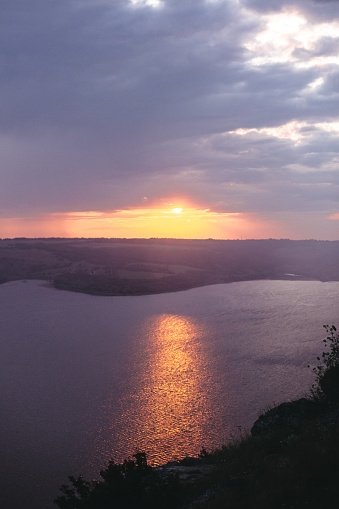 Beautiful view of sunset warm light from dark clouds above lake. Sunny rays over hill and river landscape. Dramatic moody scenery. Bakota lake and Dniester river in Ukraine