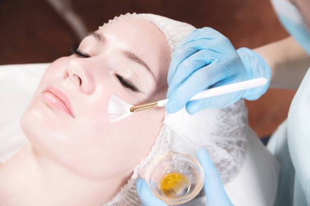 Girl beautician applies a brush to rejuvenate a mask on the face of an attractive girl in a spa salon. The concept of self-care and rejuvenation stock photo