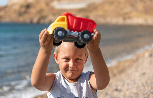 blonde boy is holding toy truck at the beach
